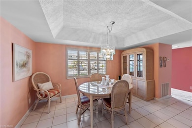 Dining area featuring a raised ceiling, plenty of natural light, light tile patterned flooring, and a textured ceiling