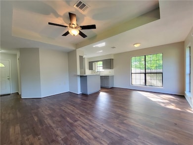 Unfurnished living room with dark wood-style floors, a ceiling fan, and a raised ceiling