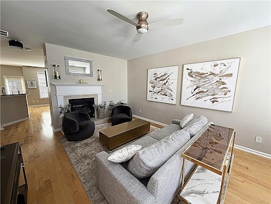 Living room with light hardwood flooring, a fireplace with raised hearth, and ceiling fan