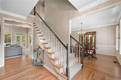 Stairs with a chandelier, french doors, wood finished floors, crown molding, and baseboards