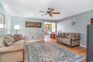 Living room featuring hardwood / wood-style floors, ceiling fan, crown molding, and wooden walls