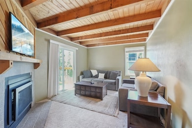 Living area with a wood ceiling with exposed beams, carpet, and a fireplace