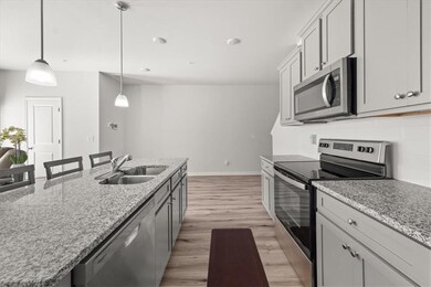 Kitchen with appliances with stainless steel finishes, light wood-style floors, hanging light fixtures, a kitchen island with sink, and light stone countertops
