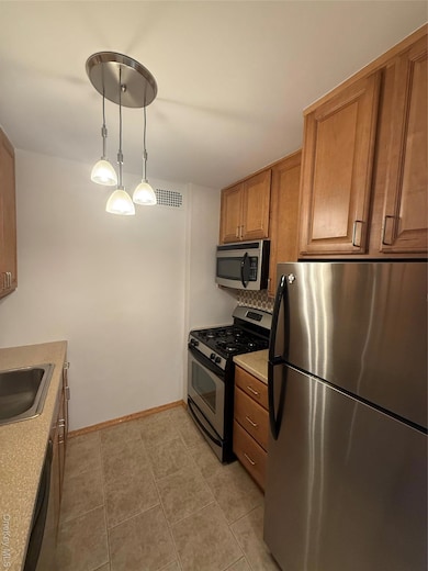 Kitchen featuring appliances with stainless steel finishes, decorative light fixtures, and brown cabinets