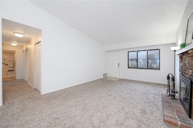 Unfurnished living room with light colored carpet, a brick fireplace, and vaulted ceiling