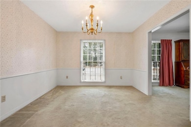 Unfurnished dining area featuring a chandelier, plenty of natural light, light carpet, a wainscoted wall, and wallpapered walls