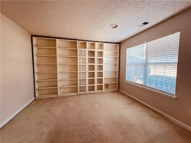 Carpeted spare room with a textured ceiling and baseboards