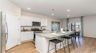 Kitchen featuring stainless steel appliances, a sink, light wood-type flooring, white cabinetry, and a center island with sink