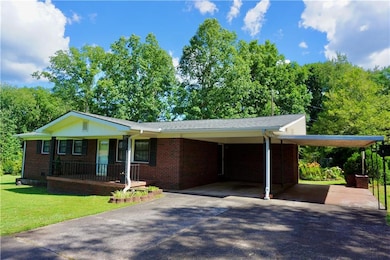 Ranch-style house with driveway, covered porch, a front yard, brick siding, and a carport