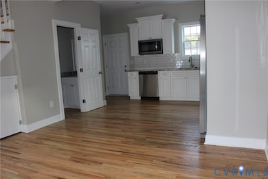 Kitchen featuring white cabinetry, stainless steel appliances, light wood-style flooring, decorative backsplash, and light stone counters