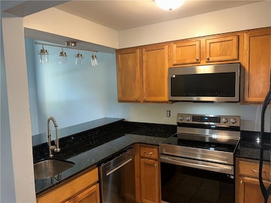 Kitchen featuring appliances with stainless steel finishes, a sink, brown cabinets, and dark stone counters