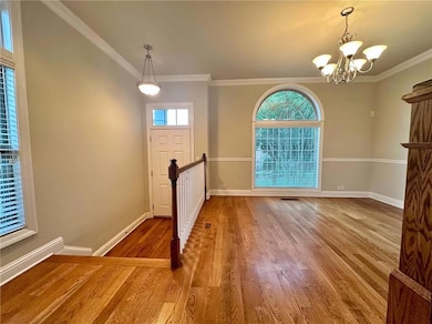 Entryway with plenty of natural light, a chandelier, baseboards, wood finished floors, and ornamental molding