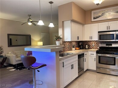 Kitchen with a breakfast bar area, appliances with stainless steel finishes, white cabinetry, hanging light fixtures, and tasteful backsplash