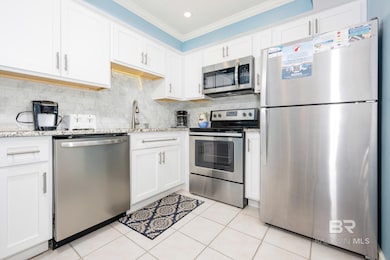 Kitchen featuring stainless steel appliances, white cabinets, light stone countertops, ornamental molding, and backsplash