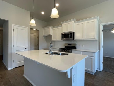 Kitchen featuring white cabinetry, appliances with stainless steel finishes, dark wood finished floors, hanging light fixtures, and a center island with sink