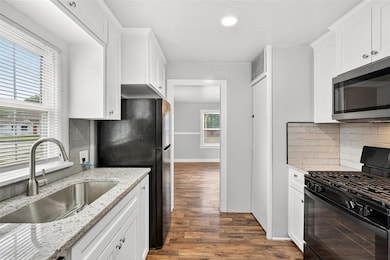 Kitchen with backsplash, black appliances, white cabinets, light stone countertops, and recessed lighting