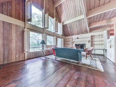 Living room with hardwood / wood-style floors, wooden walls, a brick fireplace, built in features, and high vaulted ceiling