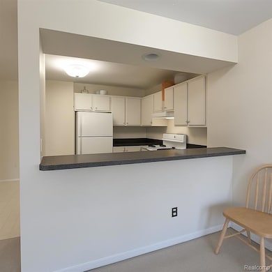 Kitchen with dark countertops, freestanding refrigerator, white cabinetry, and range
