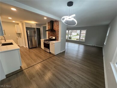Kitchen featuring wall chimney exhaust hood, hanging light fixtures, sink, stainless steel appliances, and dark hardwood / wood-style floors