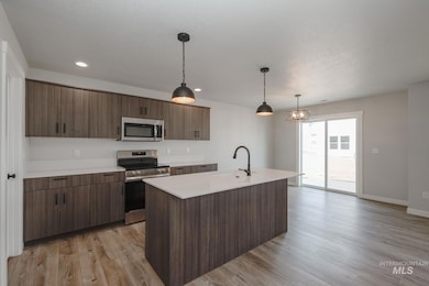 Kitchen with appliances with stainless steel finishes, hanging light fixtures, light wood-type flooring, an island with sink, and dark brown cabinets