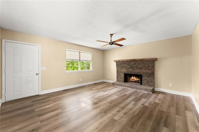 Unfurnished living room with ceiling fan, a brick fireplace, a textured ceiling, and wood finished floors