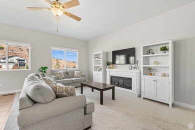 Living area with a glass covered fireplace, ceiling fan, and light carpet