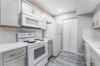 Kitchen featuring white appliances, light wood-type flooring, light stone counters, and tasteful backsplash