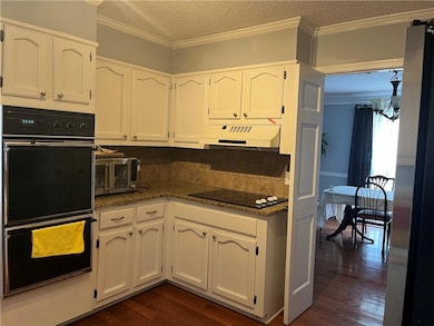 Kitchen with black appliances, extractor fan, white cabinets, dark wood-style flooring, and a textured ceiling