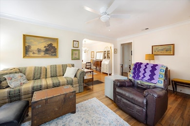 Living room featuring ornamental molding, wood finished floors, a ceiling fan, a chandelier, and arched walkways