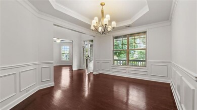 Empty room with a chandelier, a decorative wall, wood finished floors, ornamental molding, and a tray ceiling