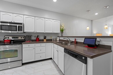 Kitchen with stainless steel appliances, a peninsula, a sink, dark countertops, and light marble finish flooring
