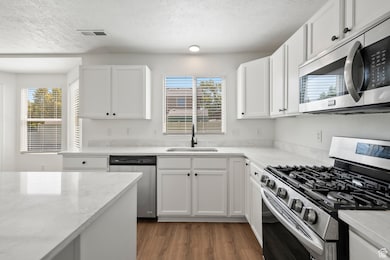 Kitchen with stainless steel appliances, a textured ceiling, white cabinetry, healthy amount of natural light, and dark wood-style flooring