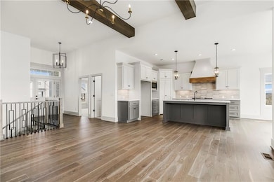 Kitchen with an inviting chandelier, premium range hood, white cabinetry, and light countertops