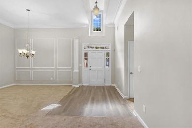Entryway featuring ornamental molding, a chandelier, light carpet, light wood-type flooring, and a towering ceiling