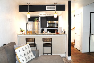 Bar area with dark cabinetry, appliances with stainless steel finishes, dark tile patterned flooring, pendant lighting, and light stone countertops