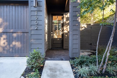 The charming entryway is framed by lush landscaping and modern details. The glass-paneled front door welcomes natural light into the home, creating an inviting transition from the serene exterior to the stylish interior.