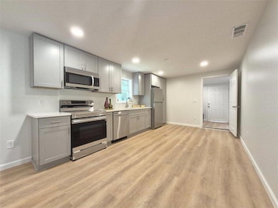 Kitchen with appliances with stainless steel finishes, gray cabinetry, light wood-style flooring, light countertops, and recessed lighting