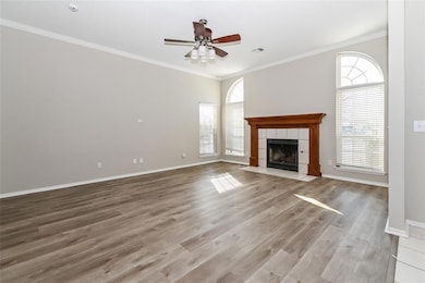 Unfurnished living room featuring ceiling fan, a tiled fireplace, ornamental molding, and a healthy amount of sunlight