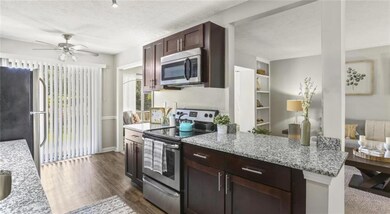 Kitchen featuring stainless steel appliances, light stone counters, ceiling fan, a textured ceiling, and dark hardwood / wood-style flooring