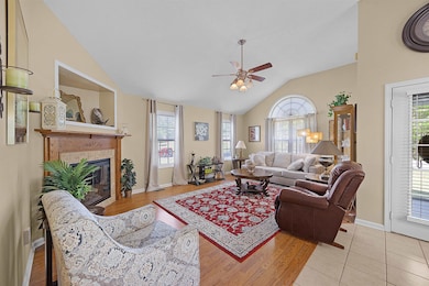 Living area featuring plenty of natural light, ceiling fan, a fireplace, and vaulted ceiling