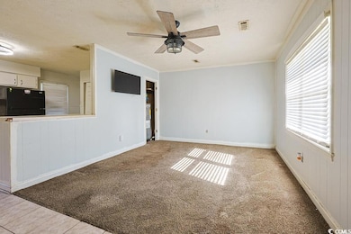 Unfurnished living room with crown molding, carpet flooring, a textured ceiling, a ceiling fan, and wooden walls