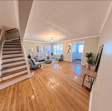 Living room featuring stairway, crown molding, light wood-style floors, and a textured ceiling