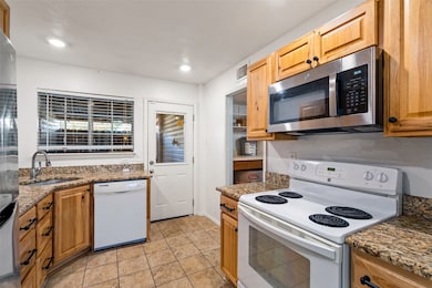 Kitchen featuring stainless steel appliances, dark stone counters, light tile patterned flooring, brown cabinetry, and recessed lighting