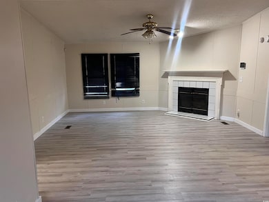 Unfurnished living room featuring a ceiling fan, wood finished floors, a textured ceiling, and a tile fireplace