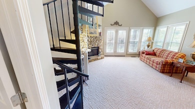 Carpeted living room featuring a stone fireplace, high vaulted ceiling, stairway, and a healthy amount of sunlight