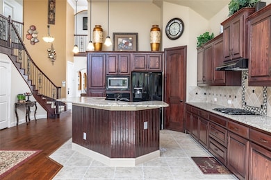 Kitchen featuring pendant lighting, high vaulted ceiling, light stone countertops, backsplash, and a kitchen island with sink