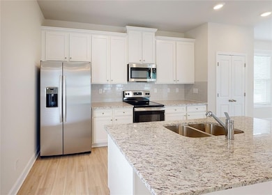 Kitchen featuring white cabinetry, stainless steel appliances, tasteful backsplash, light stone countertops, and sink