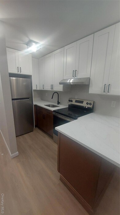 Kitchen with white cabinets, appliances with stainless steel finishes, light wood-style flooring, range hood, and light stone countertops
