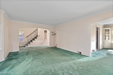 Unfurnished living room featuring arched walkways, ornamental molding, stairs, and carpet