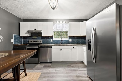 Kitchen with stainless steel appliances, white cabinets, light wood-style floors, a textured ceiling, and decorative backsplash